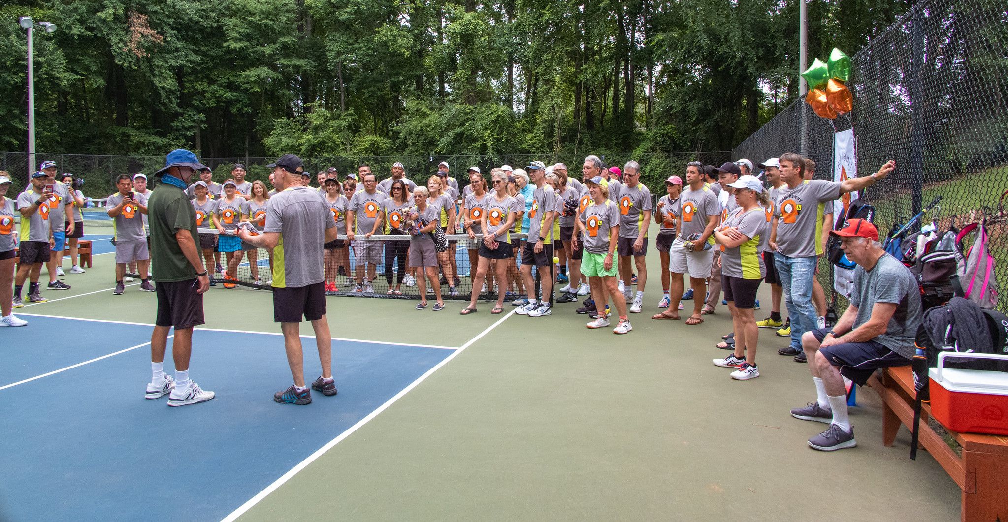 Group of people standing to the side of a pickleball court