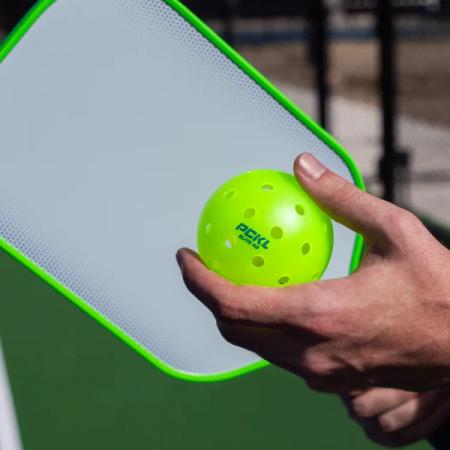 Player holding the PCKL Elite 40 pickleball ball with a PCKL paddle