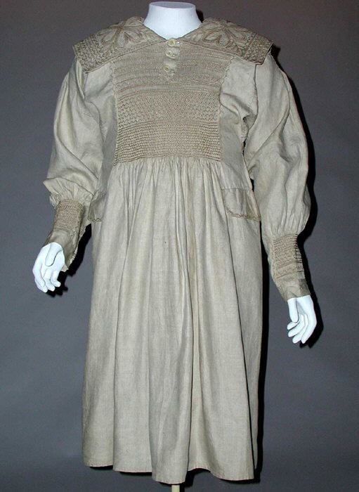 A man's linen smock of the mid to late 19th century on a mannequin, with a wide embroidered collar and a panel of smocking across the chest above a full gathered skirt.