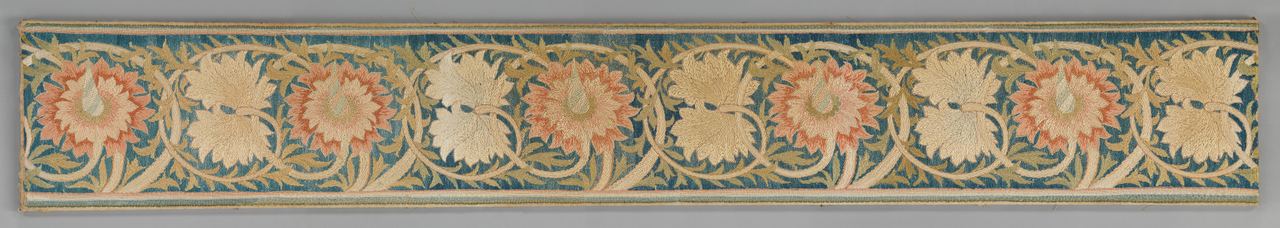 A long, narrow border of silk embroidery on a teal-blue ground: a repeating vine of curling cream stems with serrated olive-green leaves, carrying large salmon-pink flowers with pointed petals alternating with pairs of cream leaf shapes. Narrow cream and green stripes run along both edges.