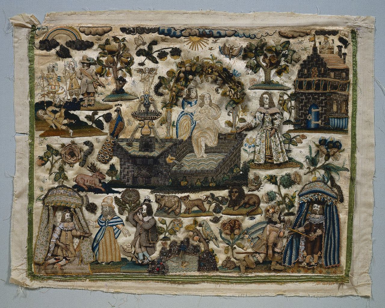 An unframed cream satin panel crowded with small embroidered figures and objects: padded men and women in seventeenth-century dress, two figures under canopies at the lower corners, two women by a pool and a stone terrace at the center, a stone building at right, a peacock, a deer, a lion and other animals, and raised leaves, trees and flowers.