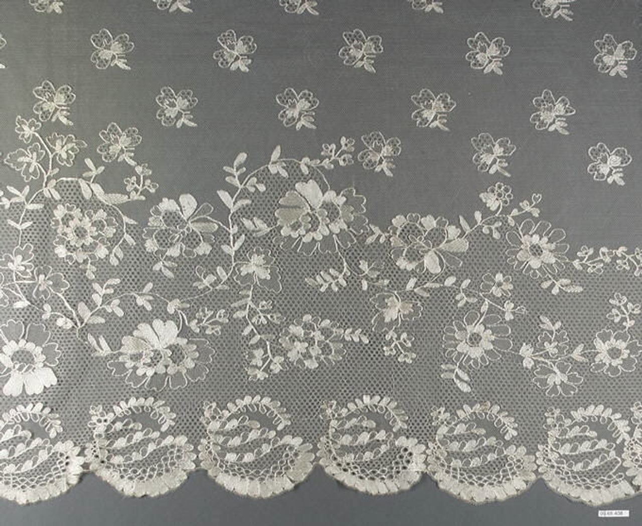 A wide flounce of fine sheer net, scattered with small floral sprigs above and with larger sprays of flowers and leaves, trailing stems and a scalloped border below, all in cream thread on gray.