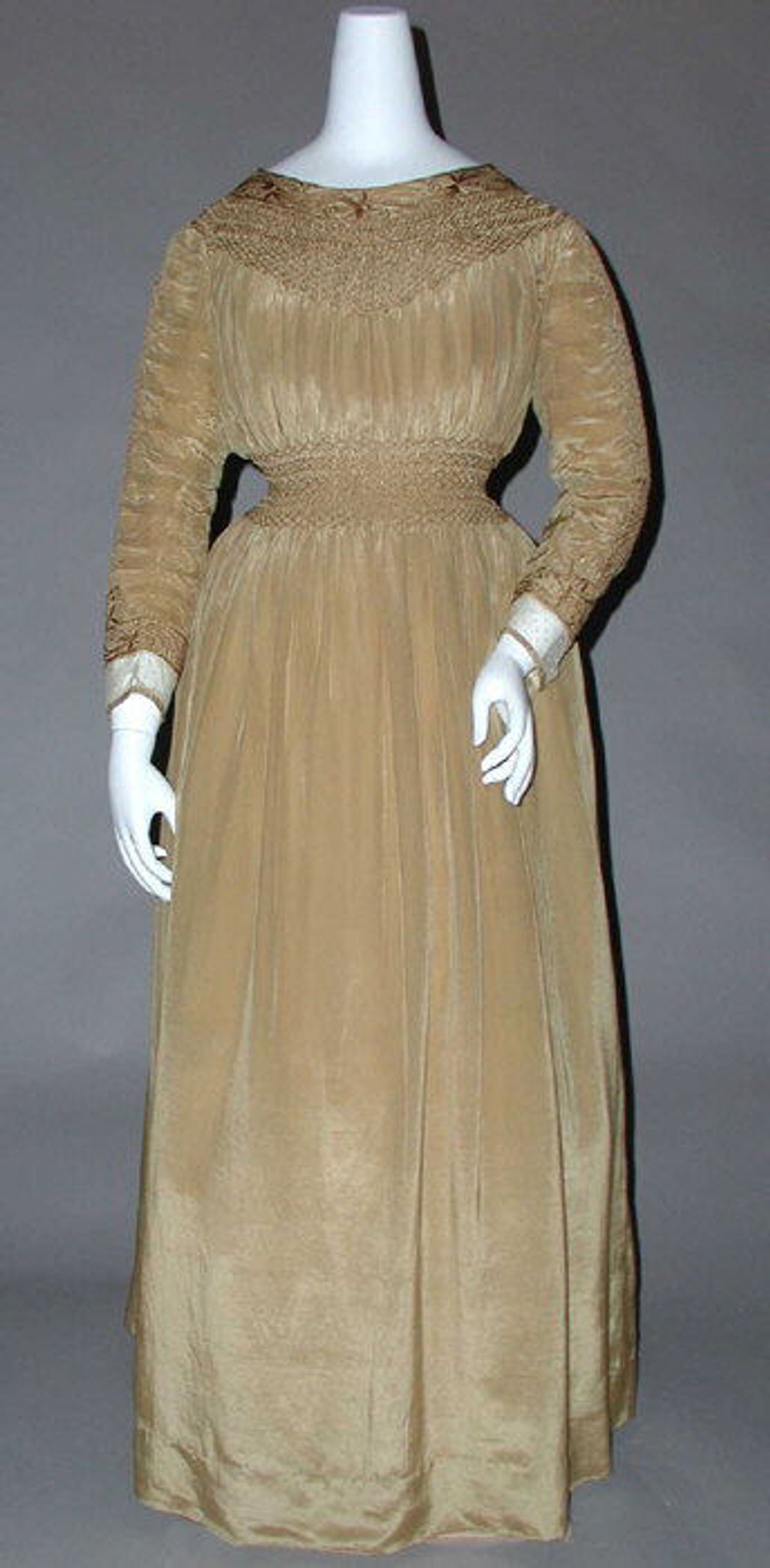 A fawn-colored dress of the 1890s on a mannequin, with smocking at the yoke and in a deep band at the waist.