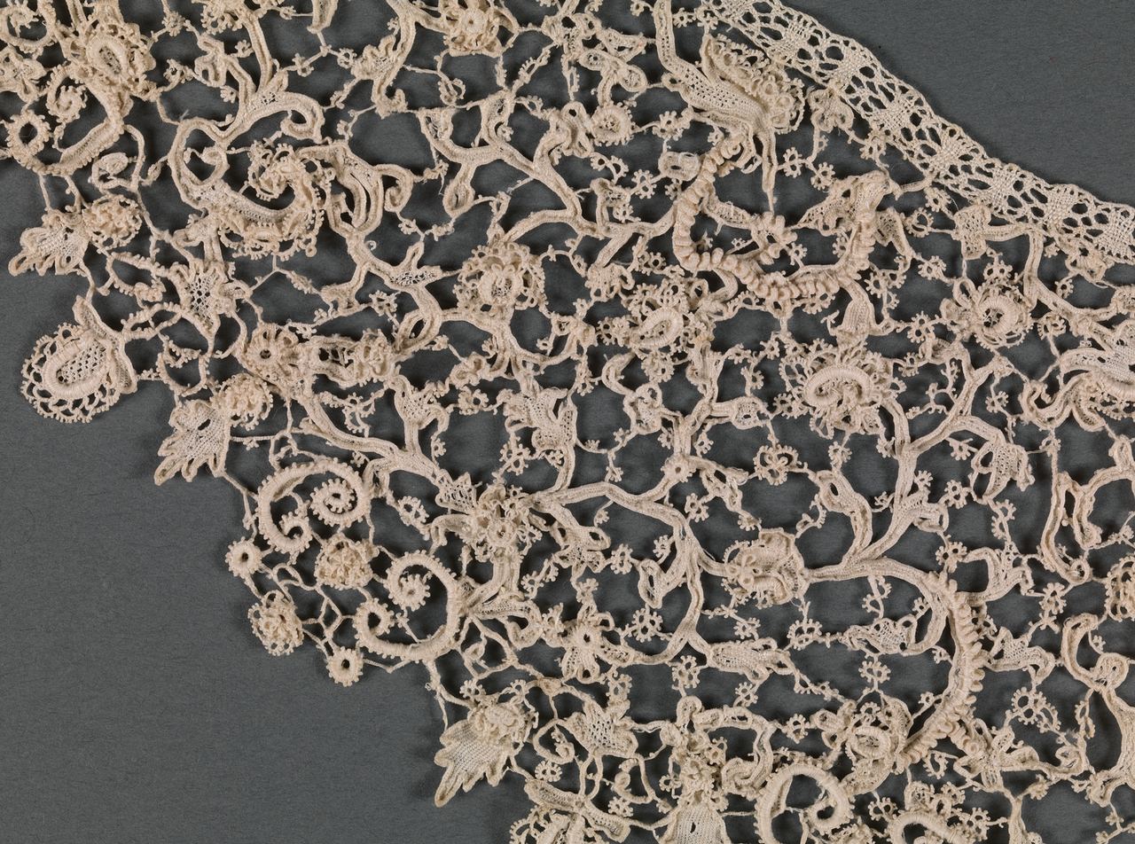 Close view of one side of the collar: raised scrolls, leaves and small flowers joined by fine bars with tiny loops, and a narrow band of straight-edged openwork along the neck edge at upper right.