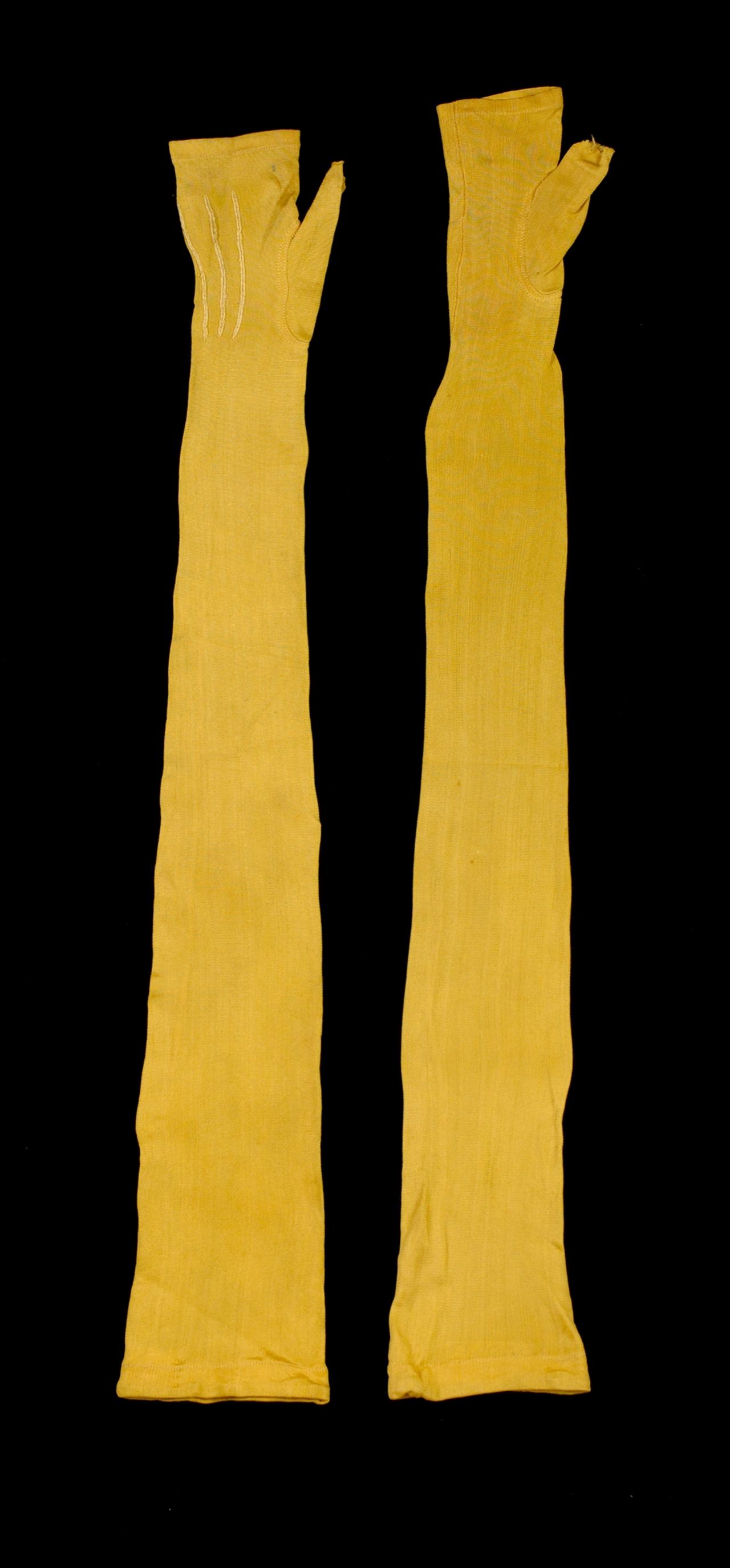 A pair of very long yellow silk mitts laid flat on black, narrow along the arm, each with a small thumb opening near the top.