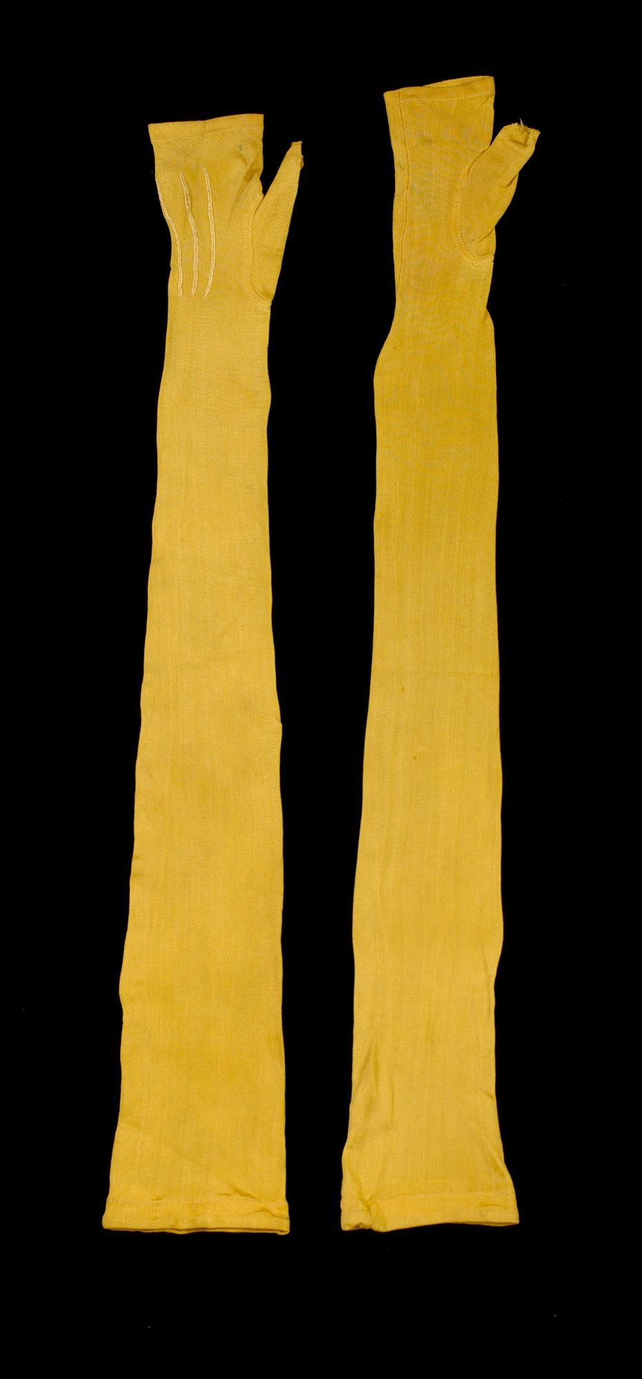 A pair of very long yellow silk mitts laid flat on black, narrow along the arm, each with a small thumb opening near the top.