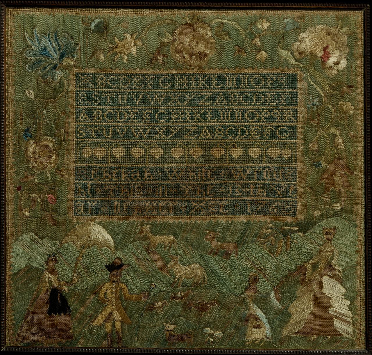 A sampler with a green and gold ground: four rows of alphabets and a row of hearts in a framed block, with flowers around it and shepherds, sheep and houses along the bottom. The letters are built from small crossed stitches.