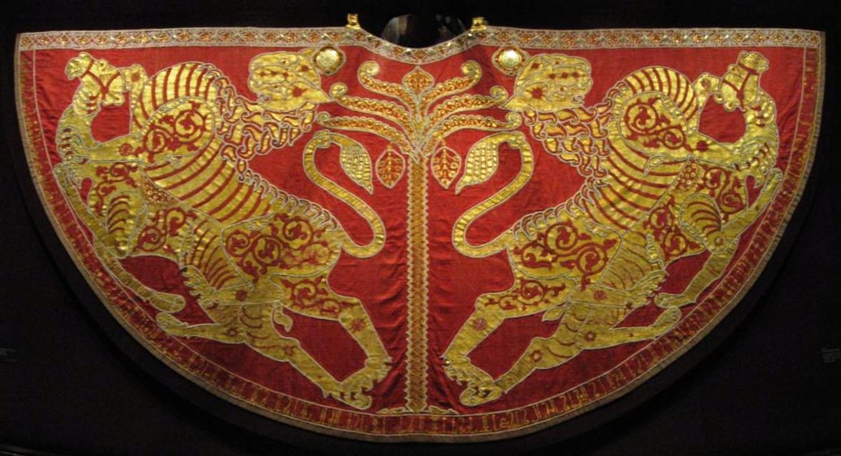 A semicircular red mantle laid flat against a dark ground. Two gold lions, embroidered in profile, face each other across a slender central tree, and a narrow border of small motifs runs along the curved lower edge.