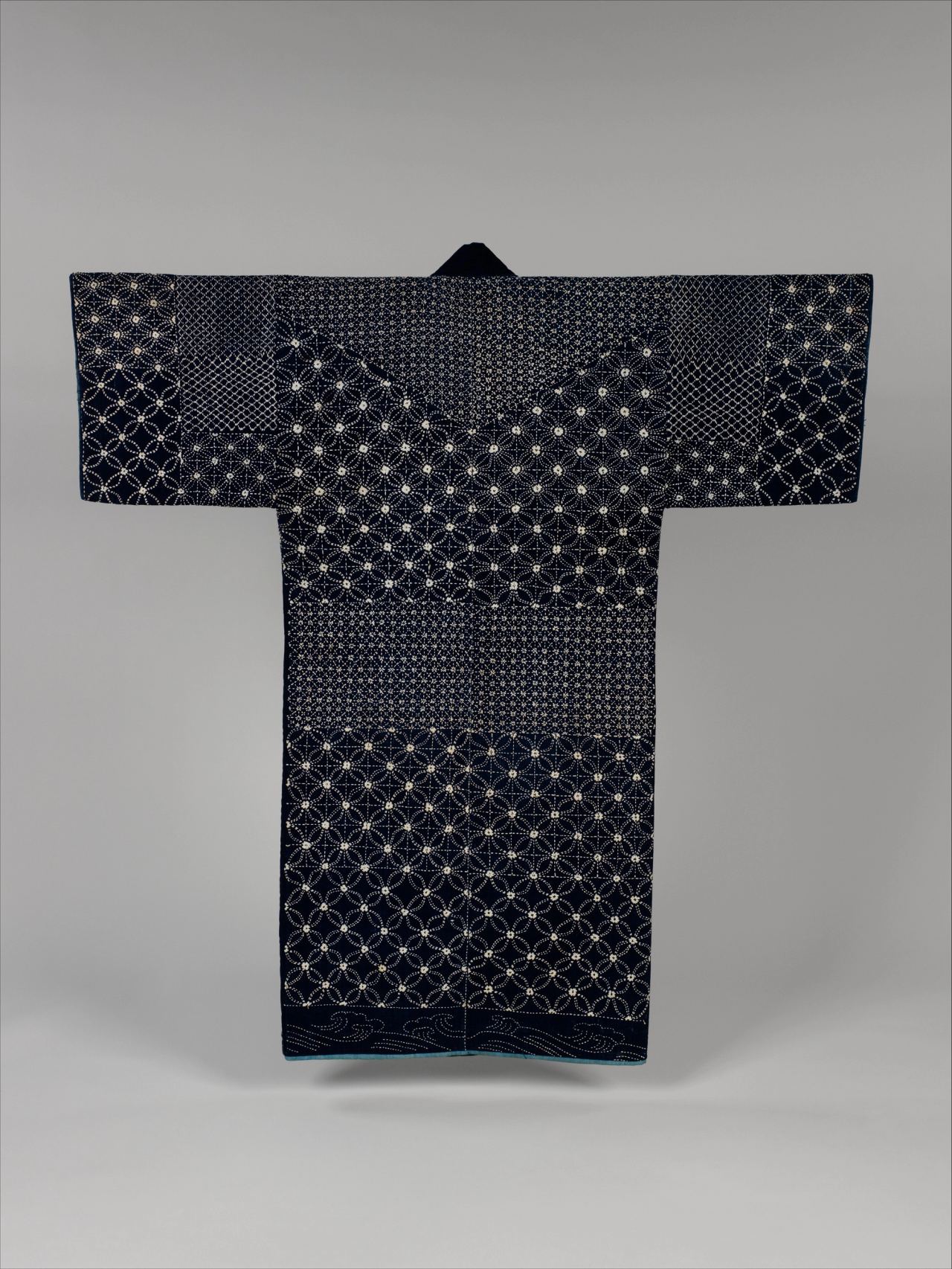 A dark indigo jacket laid flat with wide sleeves, covered in rows of white stitching that form interlocking circles and small grids.