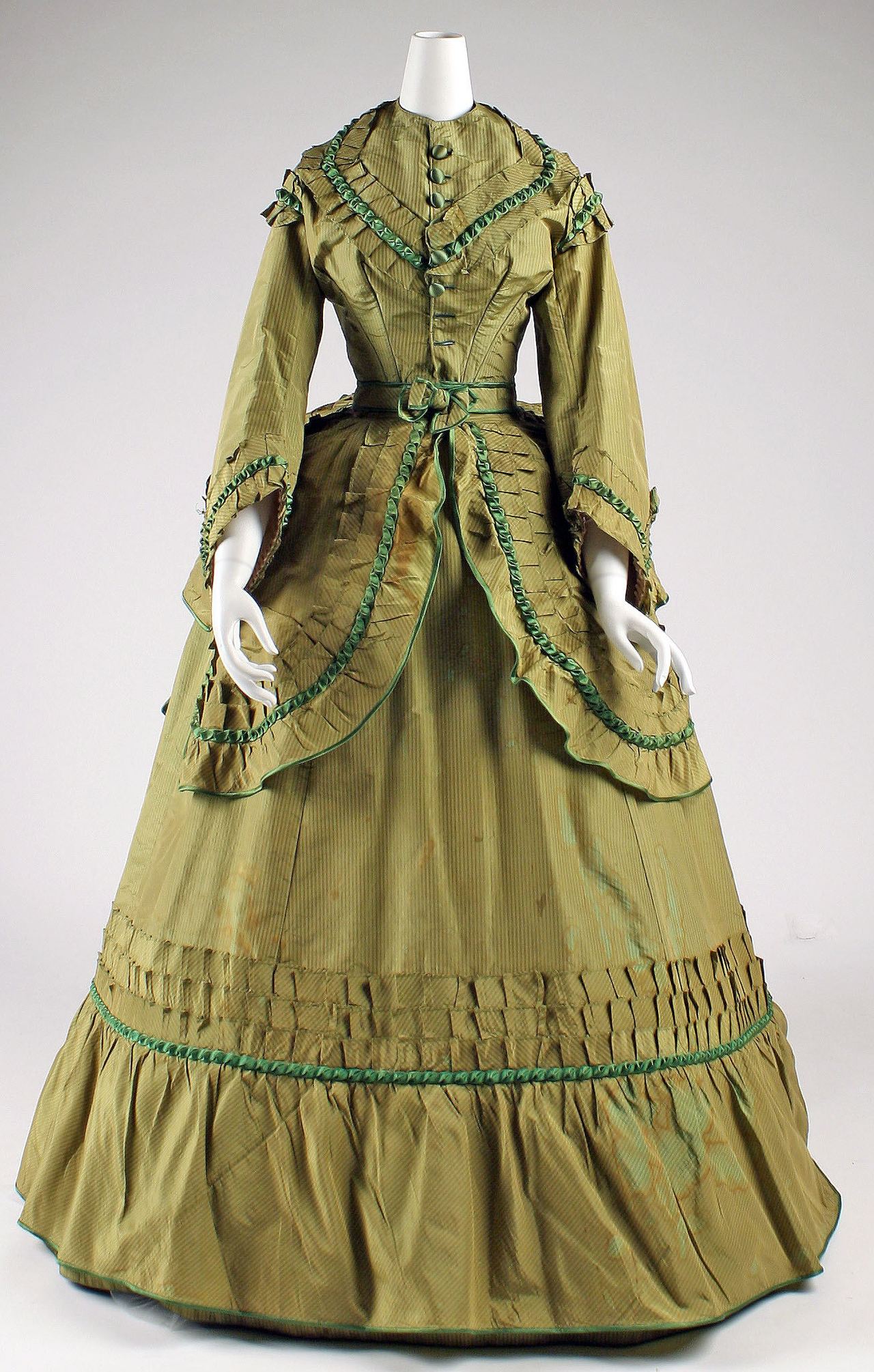 A woman's olive-green striped silk day dress on a mannequin, with a fitted bodice closing down the center front with fabric-covered buttons, bell-shaped sleeves, and a skirt trimmed with pleated bands and green ribbon.