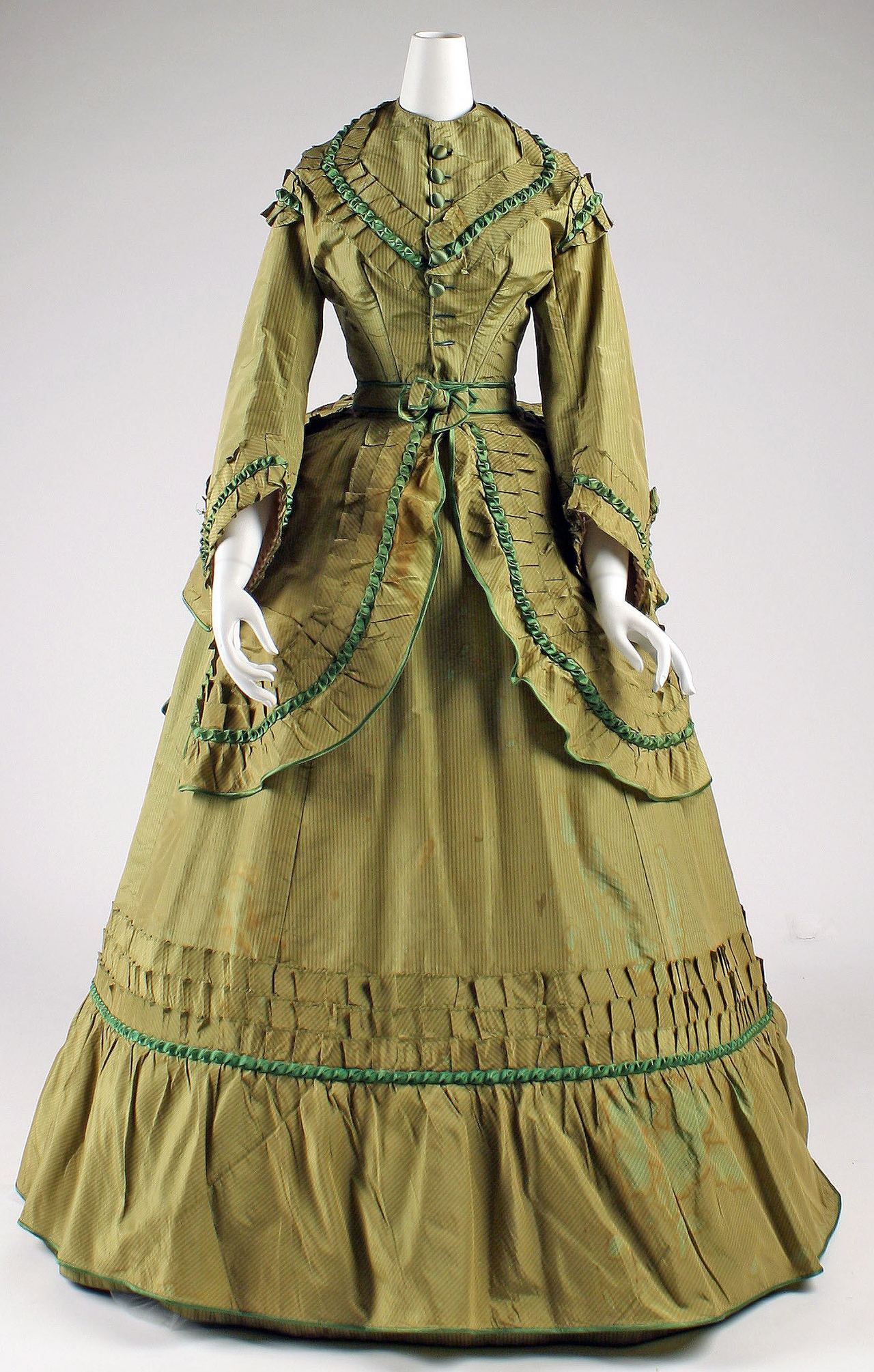 A woman's olive-green striped silk day dress on a mannequin, with a fitted bodice closing down the center front with fabric-covered buttons, bell-shaped sleeves, and a skirt trimmed with pleated bands and green ribbon.