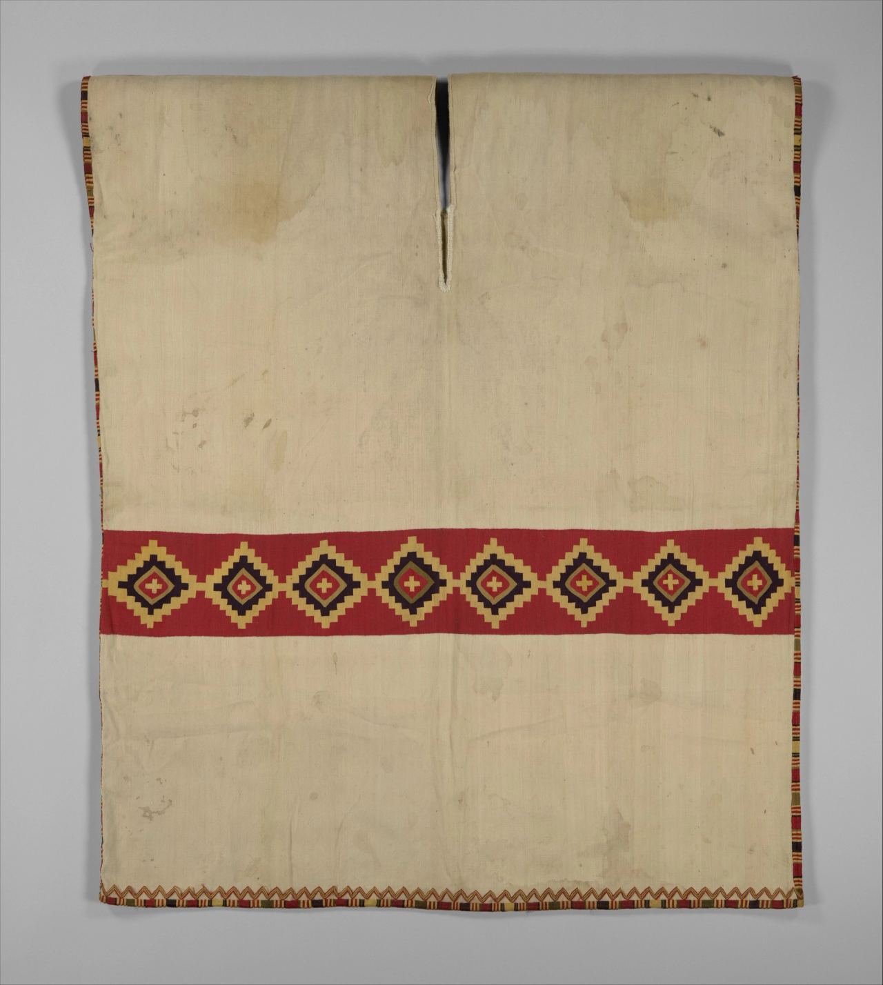 A cream tunic with a single red band across the waist holding eight stepped diamonds, shown flat.