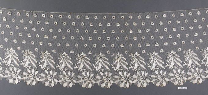 A wide border of sheer net with rows of small daisy-like dots above and a band of leaf sprays and large flowers in cream thread along a scalloped lower edge, on gray.