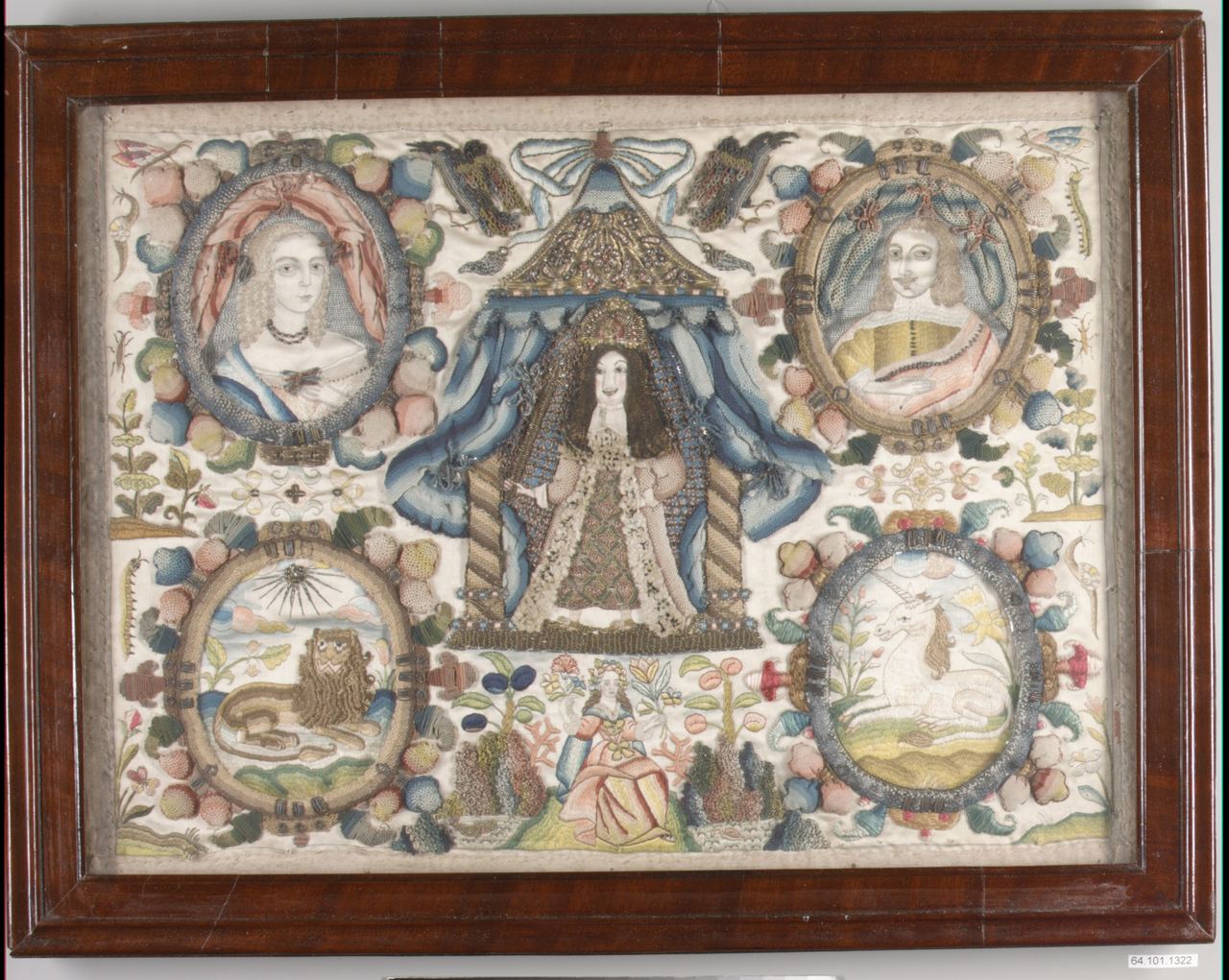 A framed embroidered picture on white silk. A crowned figure with long hair stands under a blue draped canopy at the center, with oval portrait medallions of a woman and a man at the upper corners, and a lion and a unicorn in oval medallions below, among flowers and fruit.