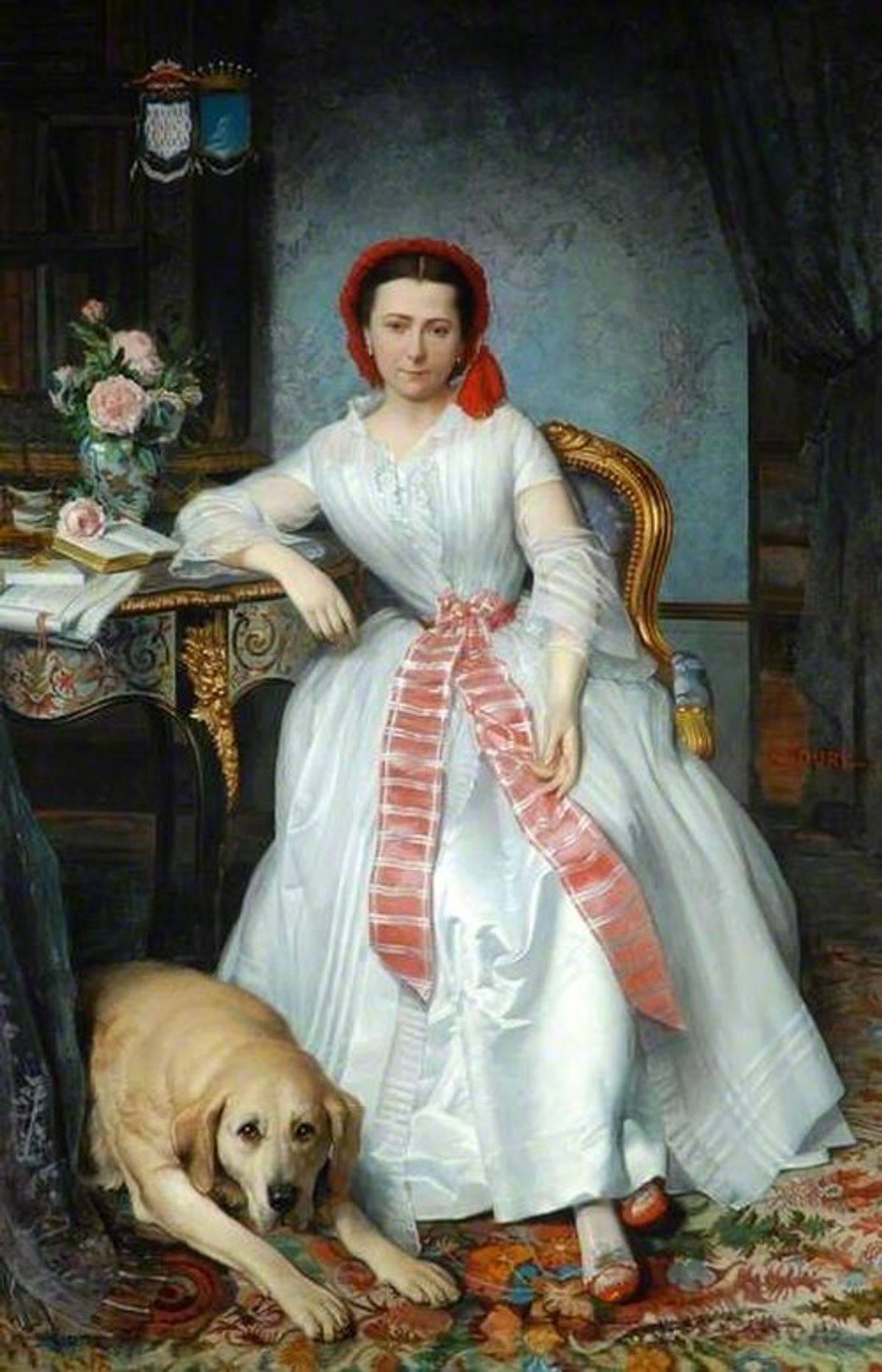 Full-length portrait of a young woman in a white silk gown with a red-and-white striped sash and a red cap, seated beside a gilt-edged table with a book, papers and a vase of roses, a large pale dog lying at her feet on a patterned carpet.
