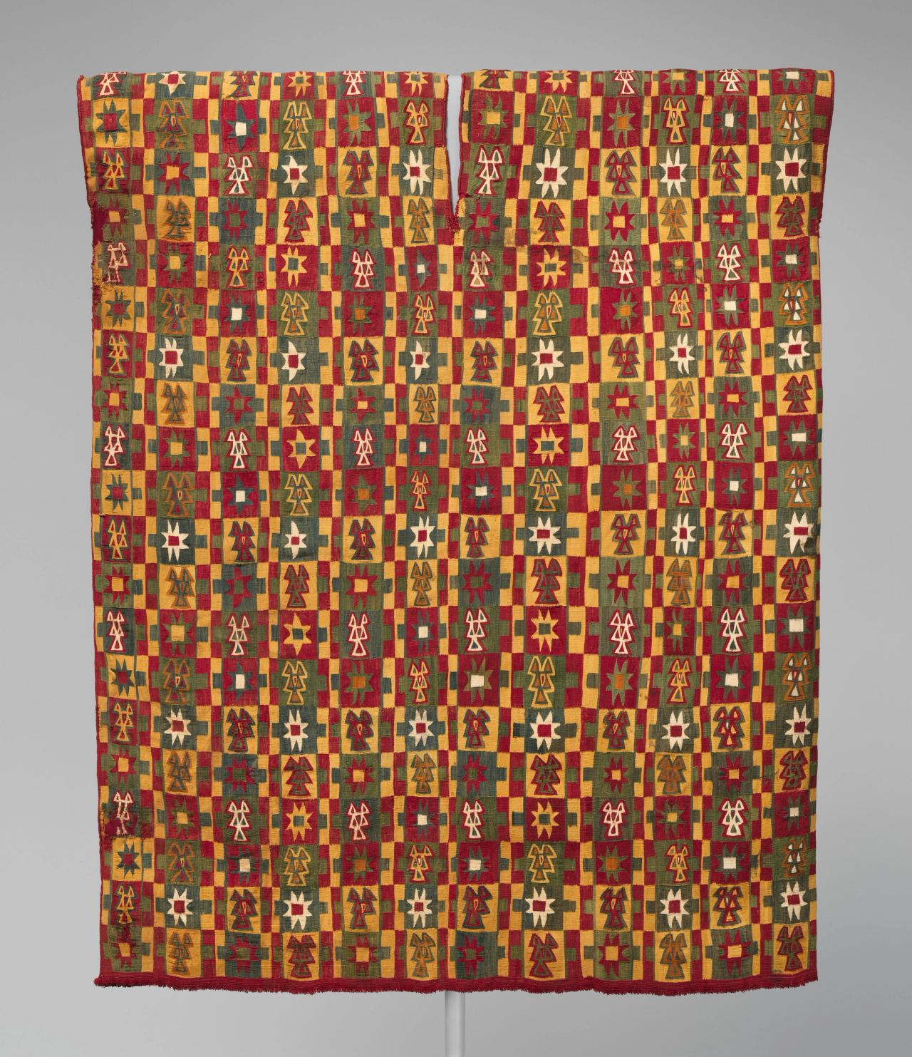 A tunic woven as a grid of red, yellow, green and cream squares, each holding a small star or bird-like motif, shown flat.