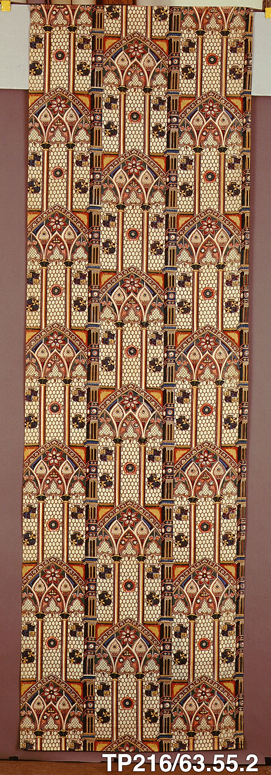 A tall narrow length of cotton printed in brown, orange, cream and black with repeating Gothic pointed arches, tracery and small flowers.