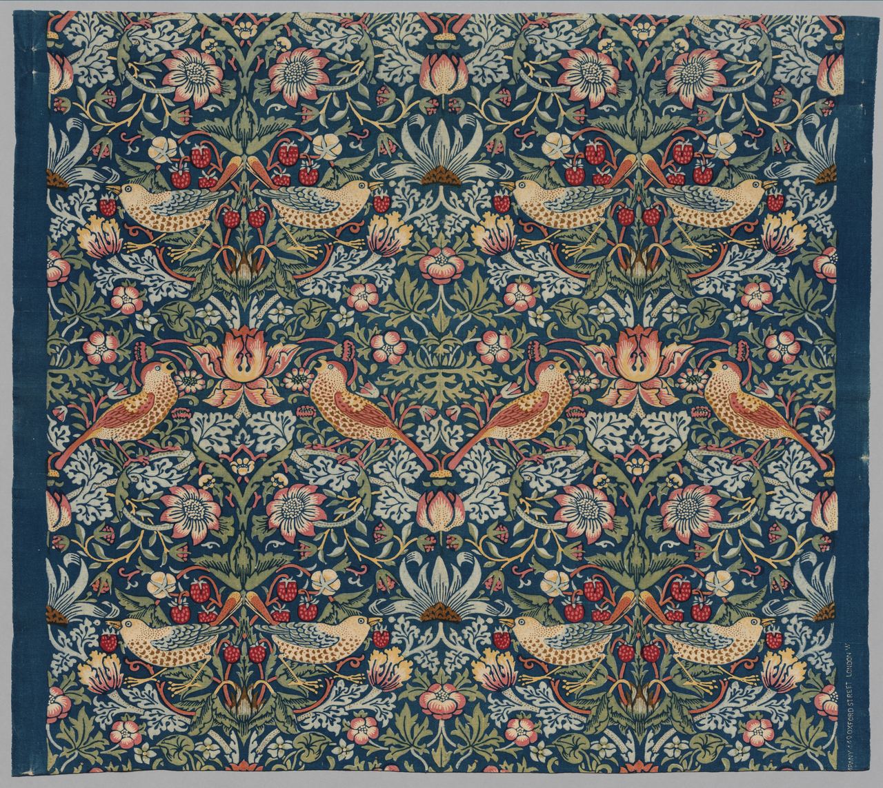 A dark blue cotton furnishing fabric printed with mirrored pairs of thrushes among strawberry plants, flowers and leaves in cream, pink, red and green.