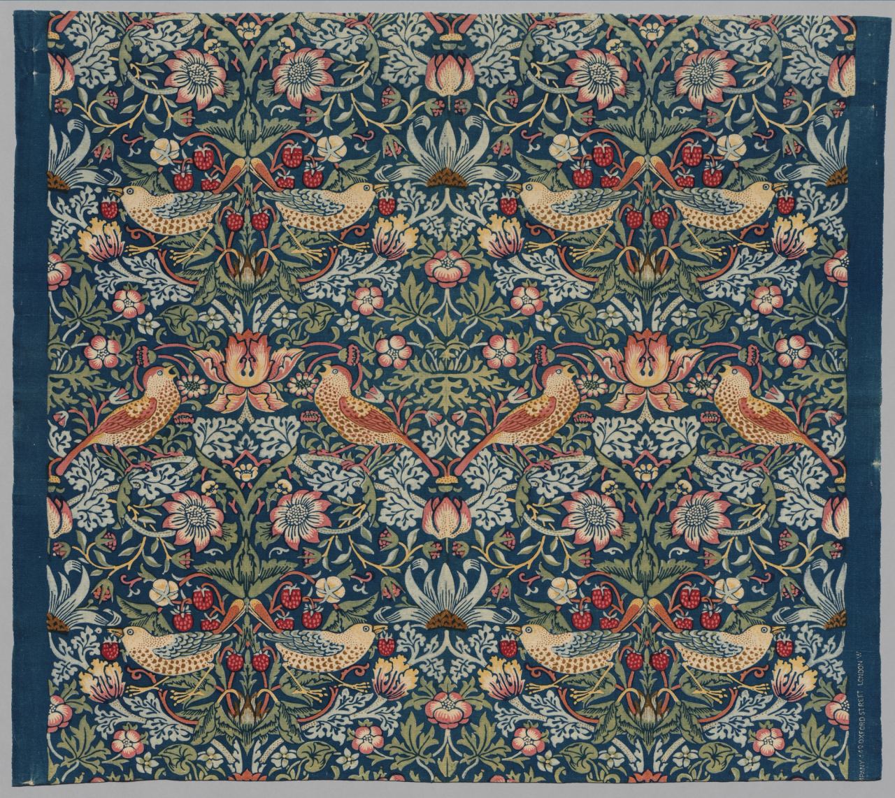 A dark blue cotton furnishing fabric printed with mirrored pairs of thrushes among strawberry plants, flowers and leaves in cream, pink, red and green.