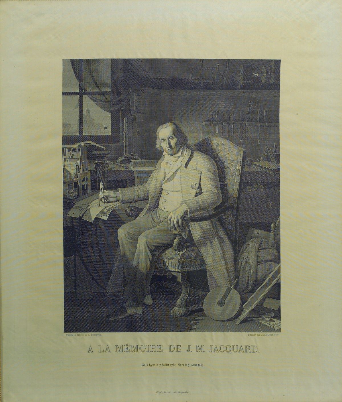 A silk portrait woven to look like an engraving. An elderly man in a long coat sits in an armchair in a workshop, a pen in his right hand over papers on a table, with tools and a small machine behind him. Woven lettering below reads A la mémoire de J. M. Jacquard, with his birth and death dates.