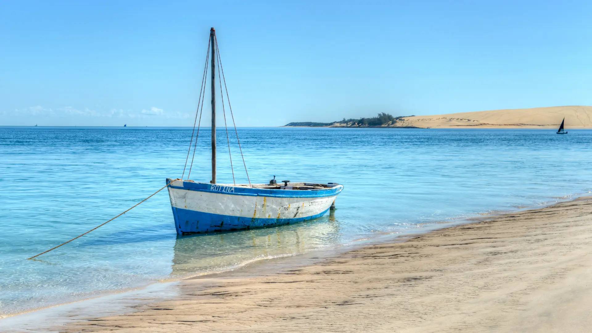 Traditional dhow anchored in shallow turquoise water along a sandy beach in Mozambique