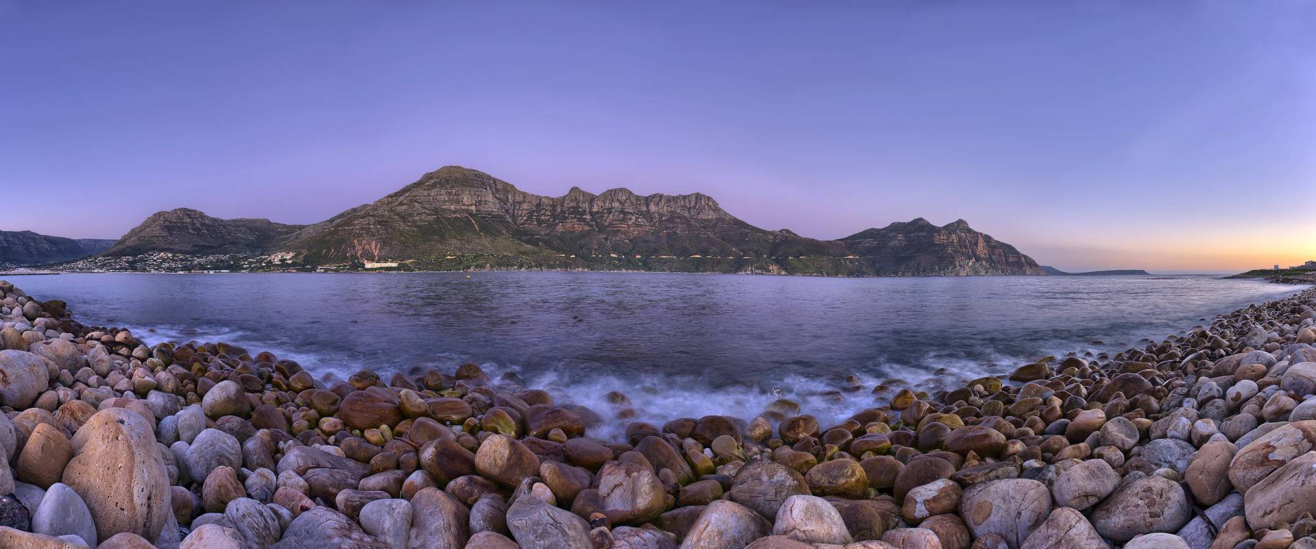 Rocky shoreline with panoramic view of Cape Town’s coastal mountains at sunset