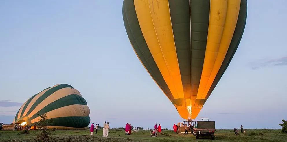 Hot air balloons being prepared for launch at dawn with people gathered on the grassland