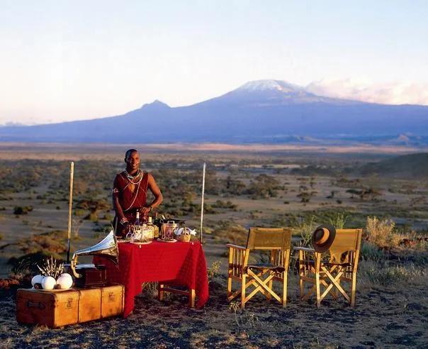 Maasai host standing beside a luxury breakfast setup with Mount Kilimanjaro in the background