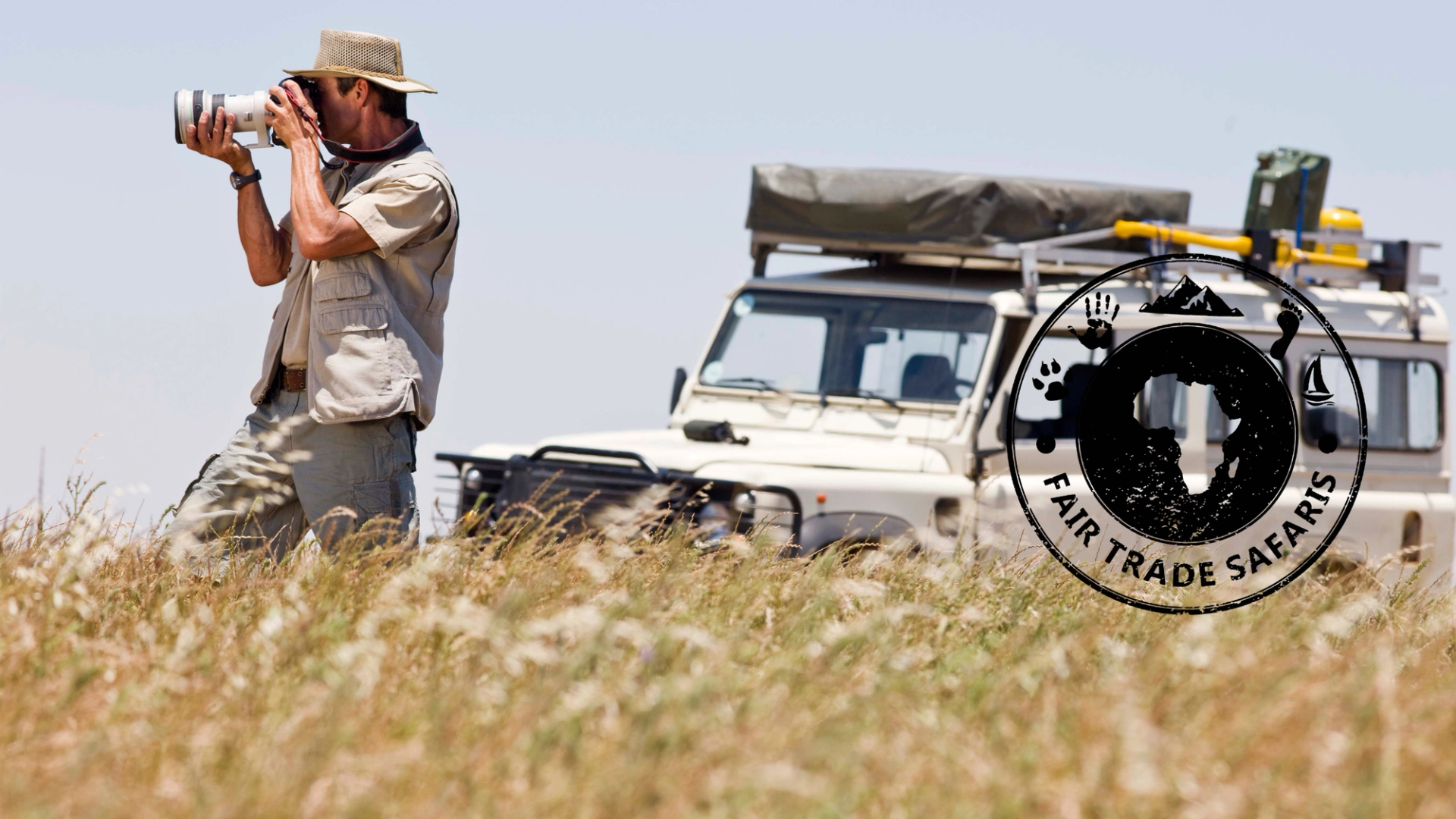 Safari guide photographing wildlife in tall grass beside a safari vehicle, with the Fair Trade Safaris logo displayed on the right.