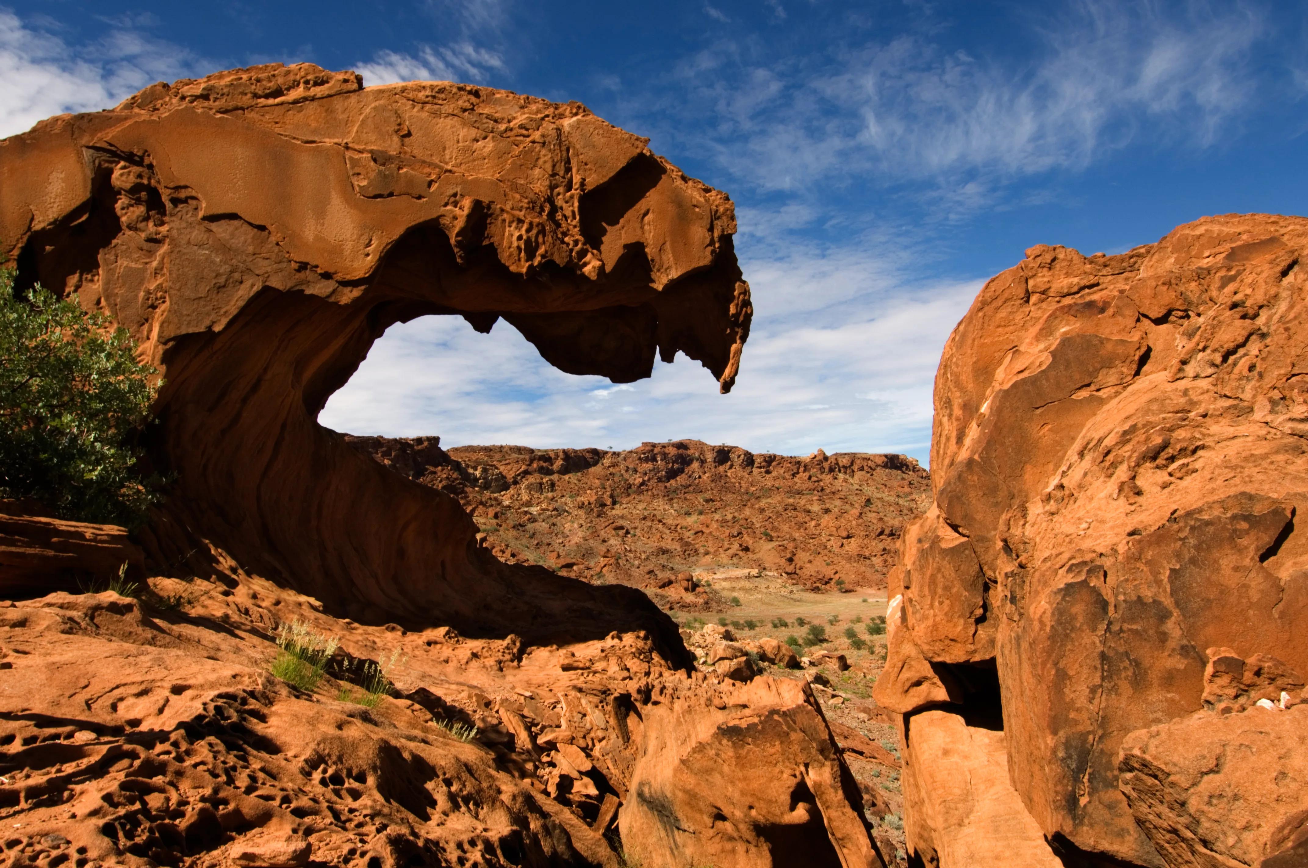 Red sandstone arch formation in the Namibian desert under a blue sky with scattered clouds