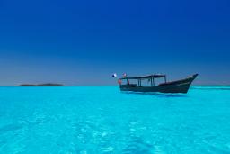 Traditional dhow floating on crystal-clear turquoise waters under a deep blue sky at Diani Beach, Kenya