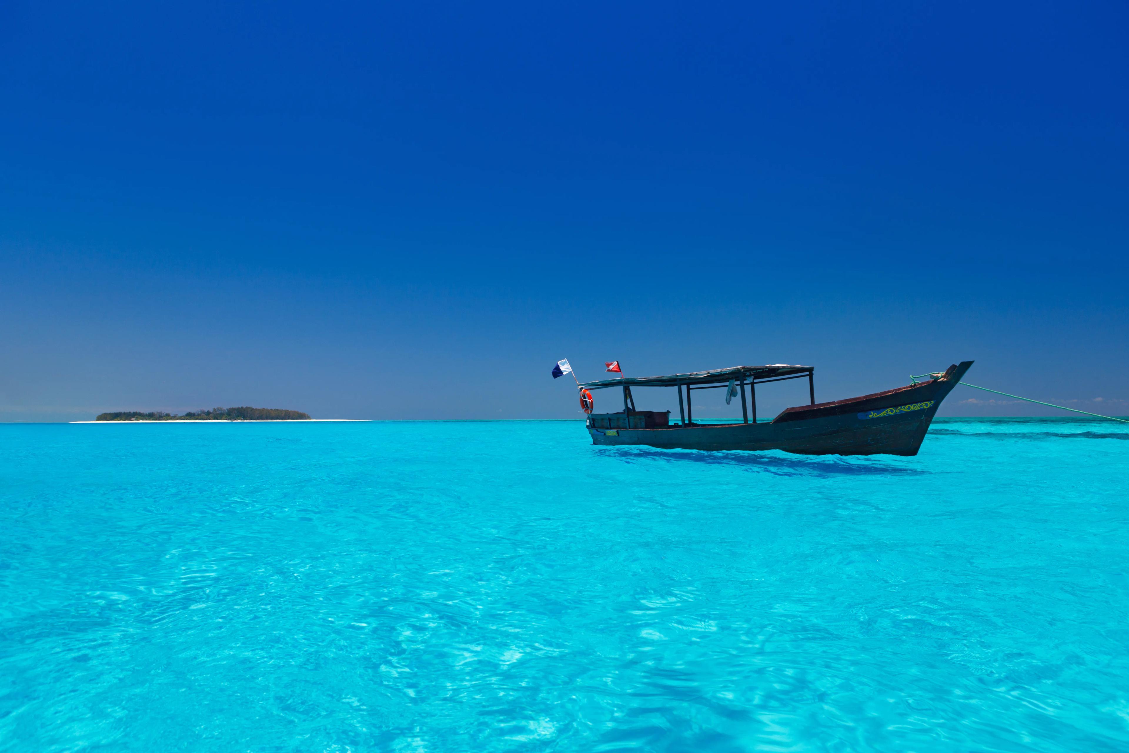 Traditional dhow floating on crystal-clear turquoise waters under a deep blue sky at Diani Beach, Kenya