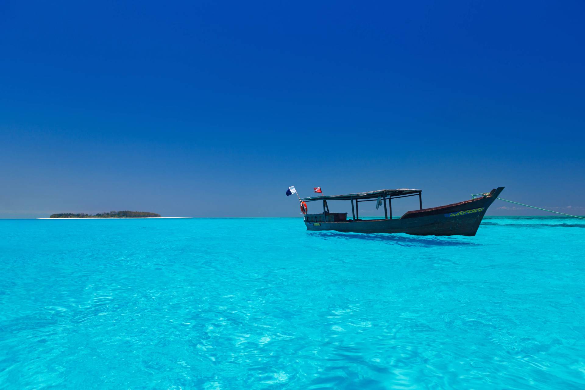 Traditional dhow floating on crystal-clear turquoise waters under a deep blue sky at Diani Beach, Kenya