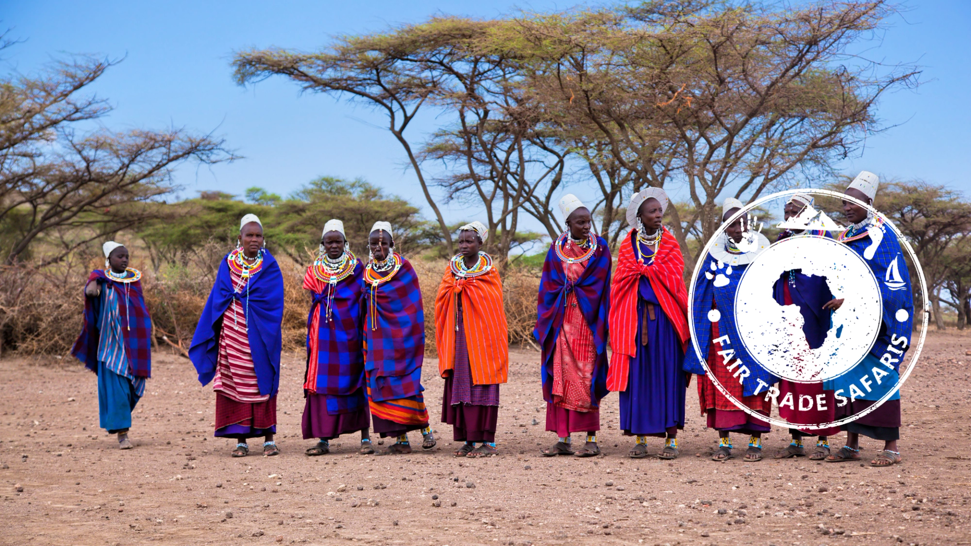 Group of Maasai women wearing colorful traditional clothing and beaded jewelry walking across a dry savanna landscape, with acacia trees in the background and the Fair Trade Safaris logo displayed on the right.
