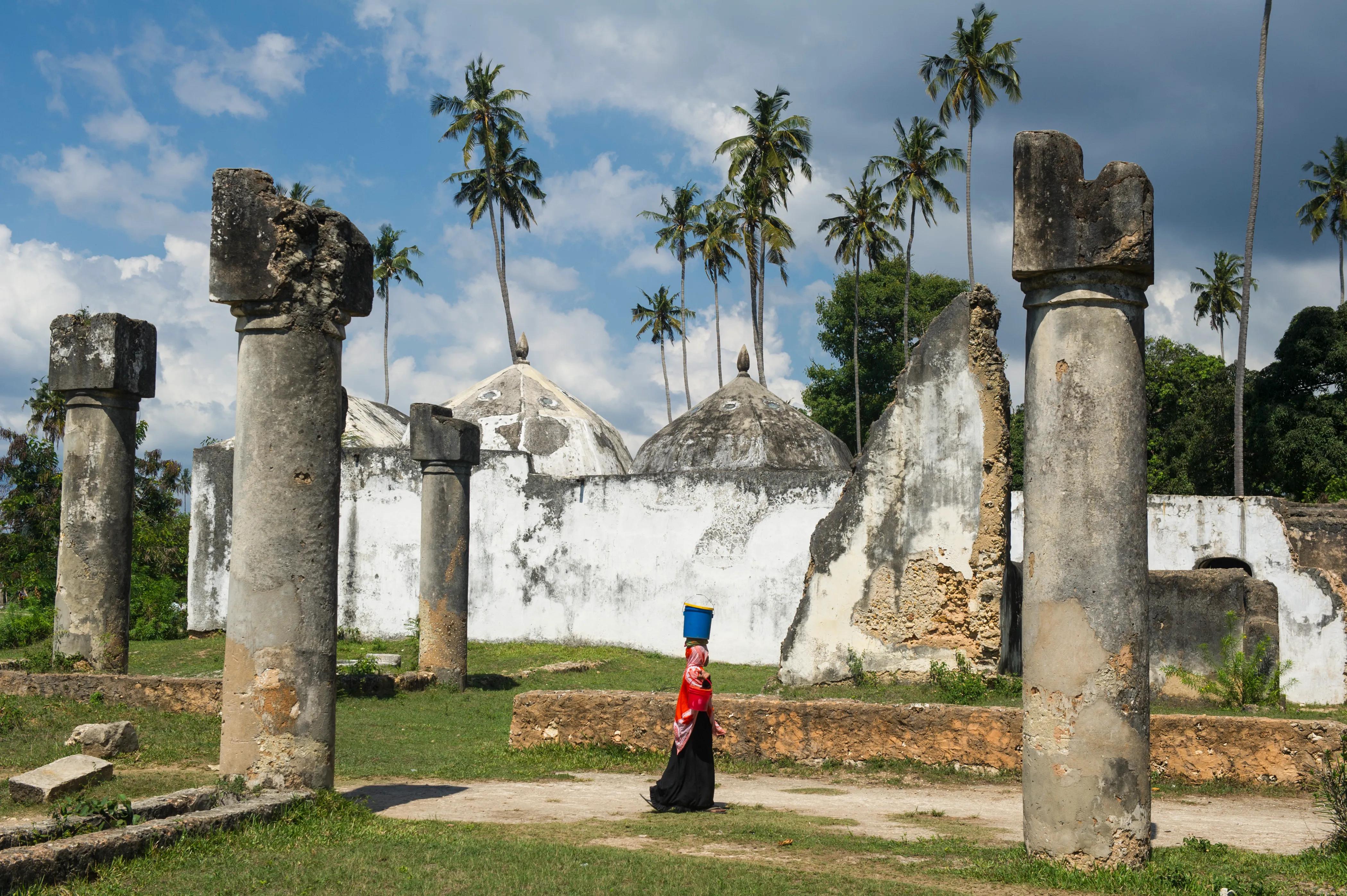 Woman in traditional dress walking through ancient Swahili ruins with palm trees in Tanzania