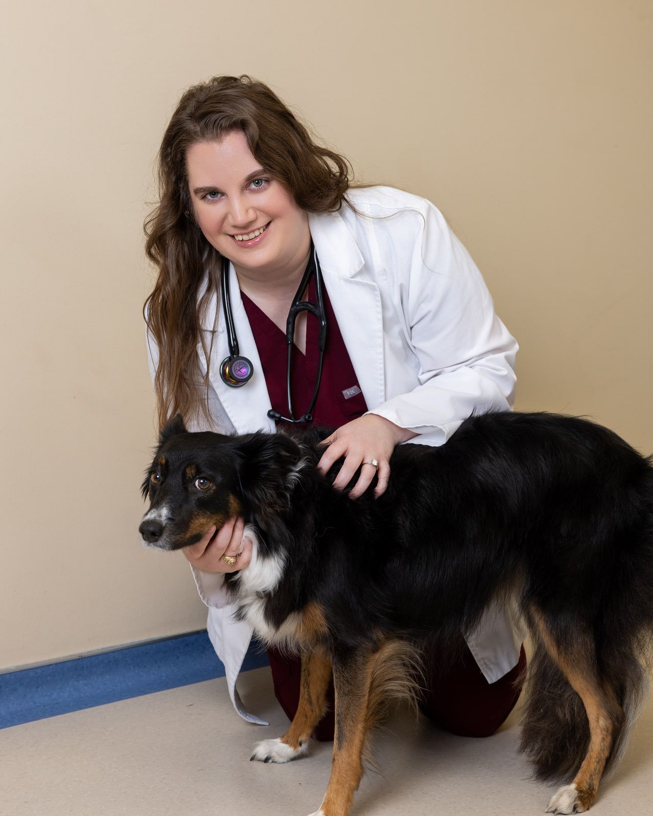 A veterinarian in a white coat kneeling beside a black-and-tan Australian Shepherd