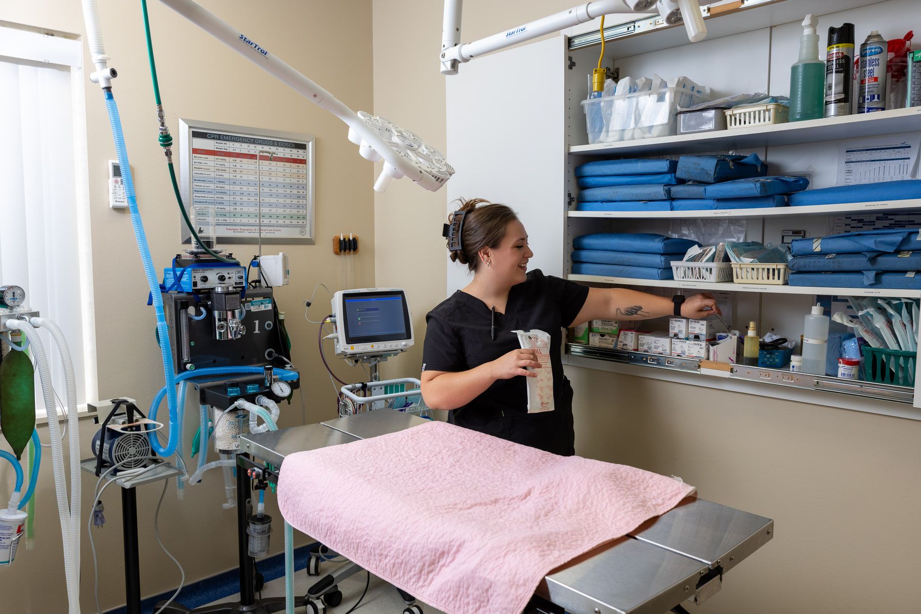 A technician preparing equipment in the surgical suite beside an anesthesia machine