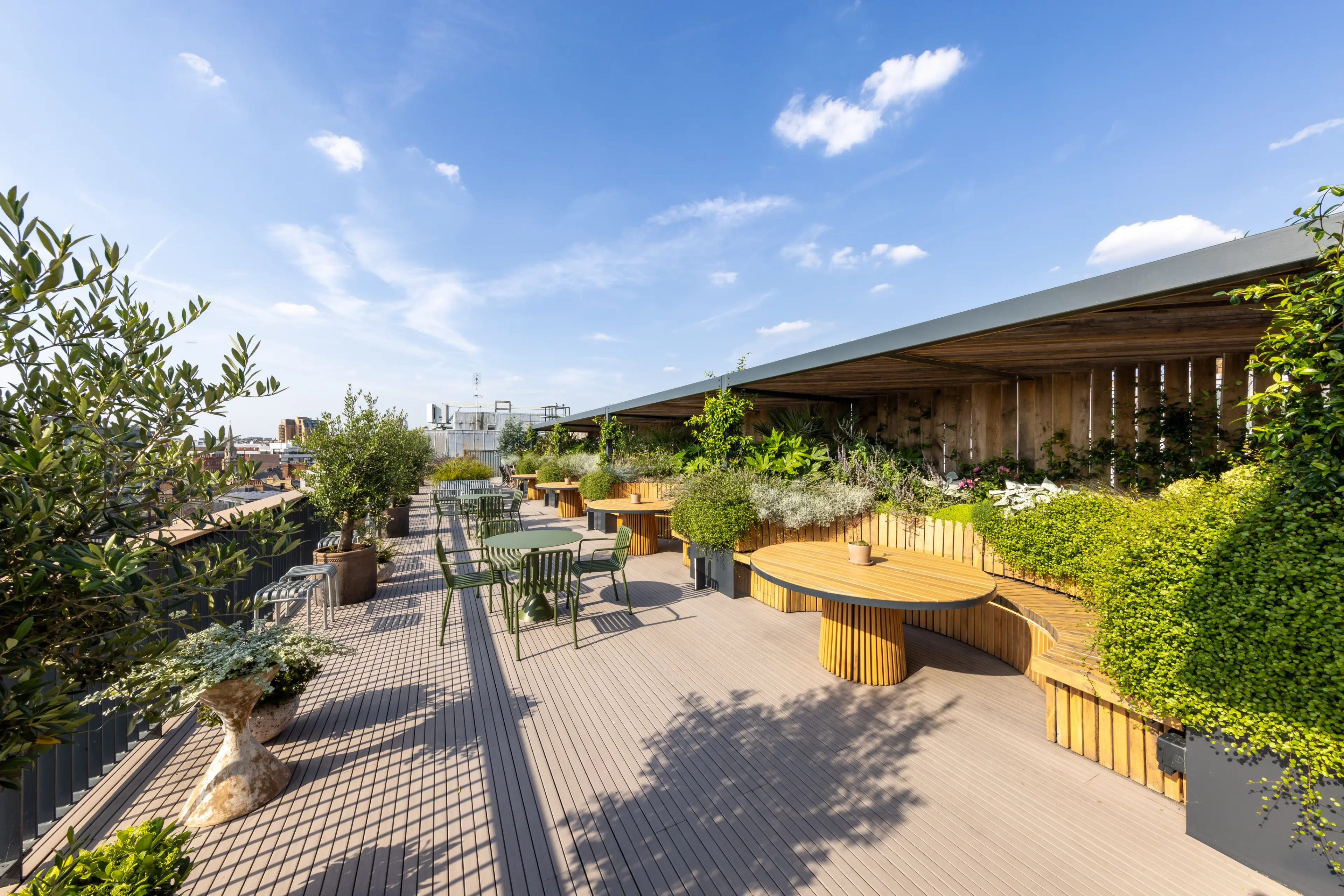 A sunny rooftop terrace with outdoor seating, wooden decking, and lush green plants.