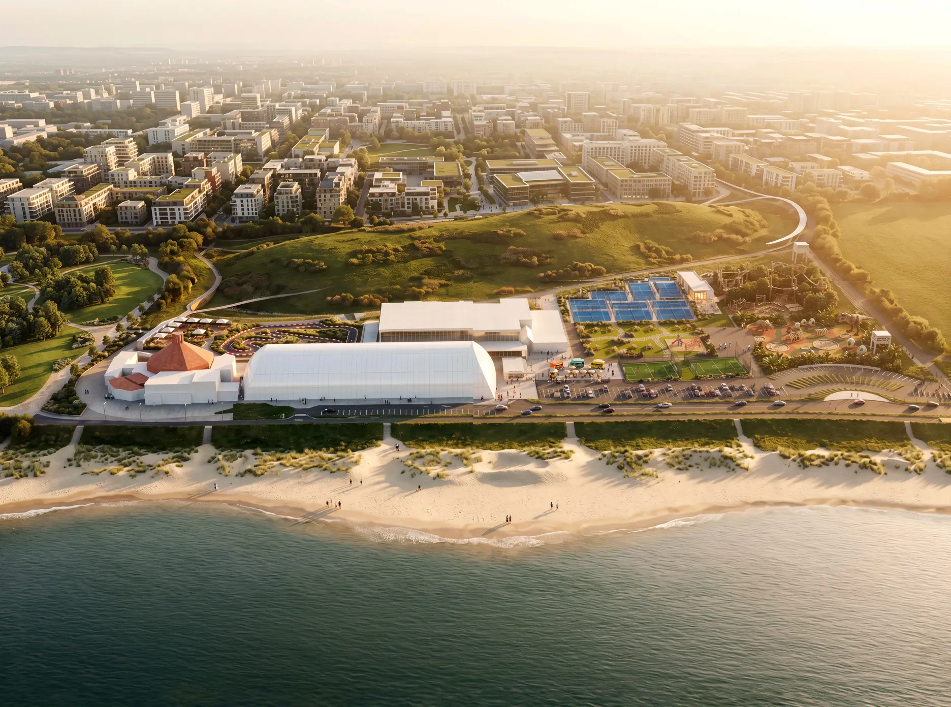 Aerial view of a large coastal development with a white sports arena, multiple tennis courts, a beach, and a city in the background.