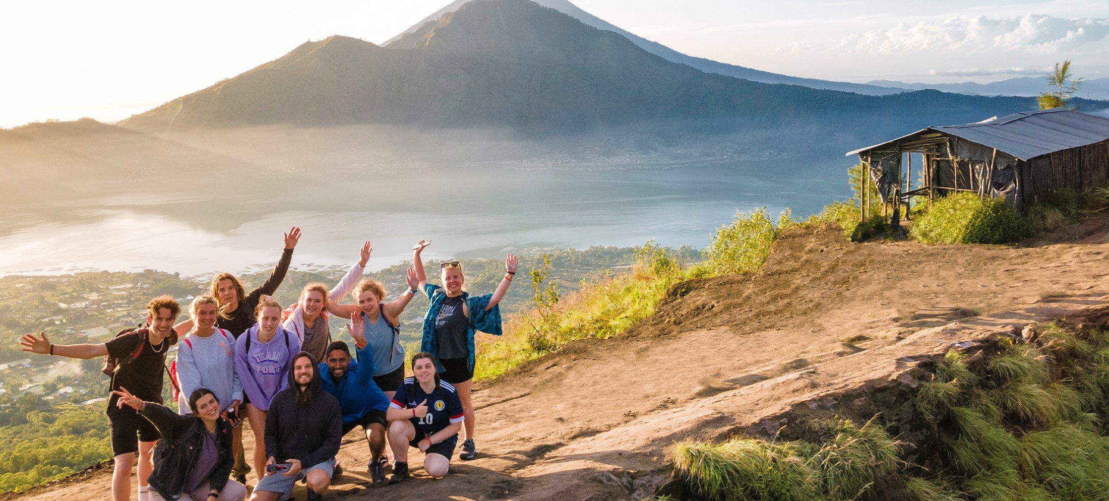 A group of travellers poses in front of Mount Batur at a look out in Bali