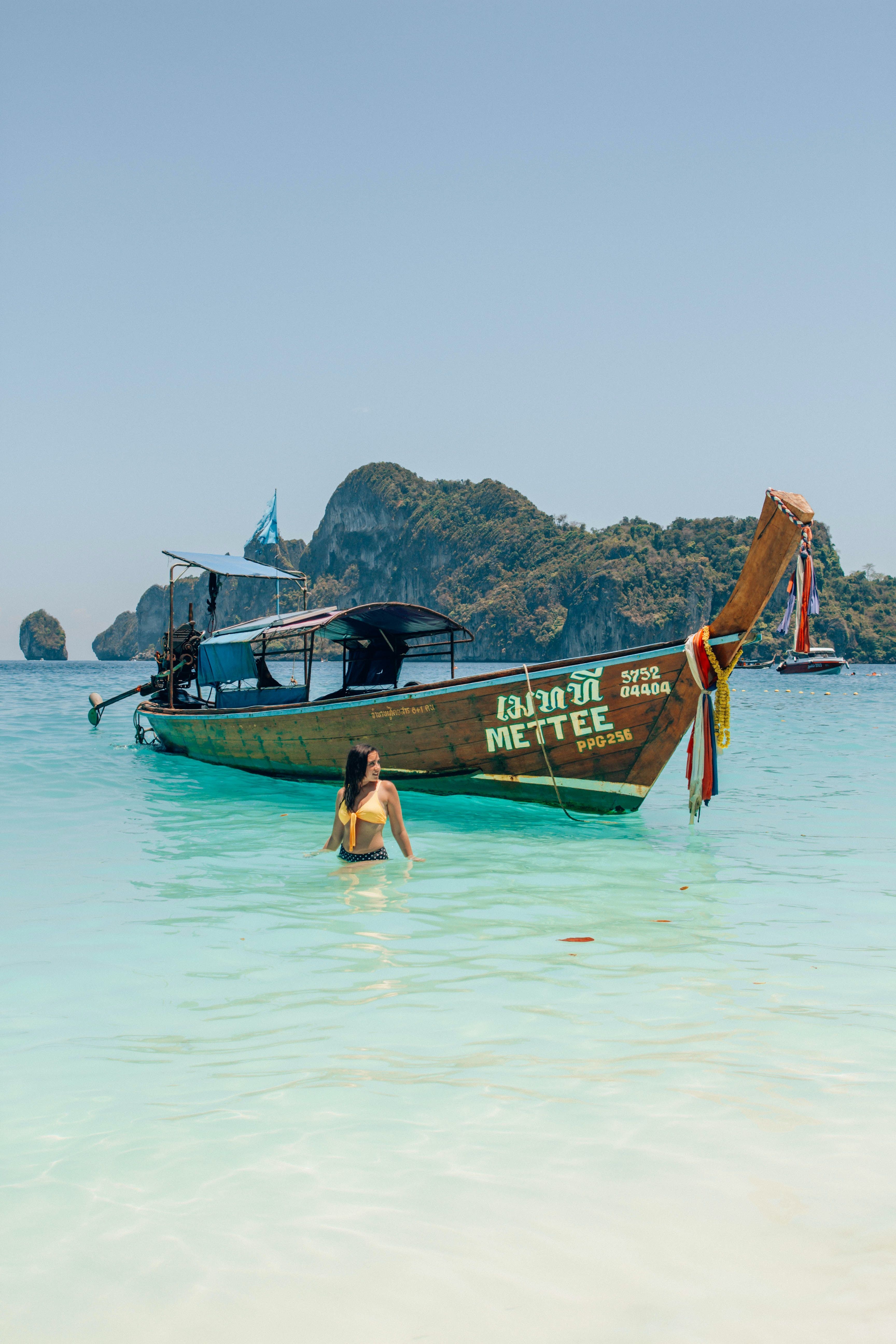 Girl swims in front of traditional Thai boat