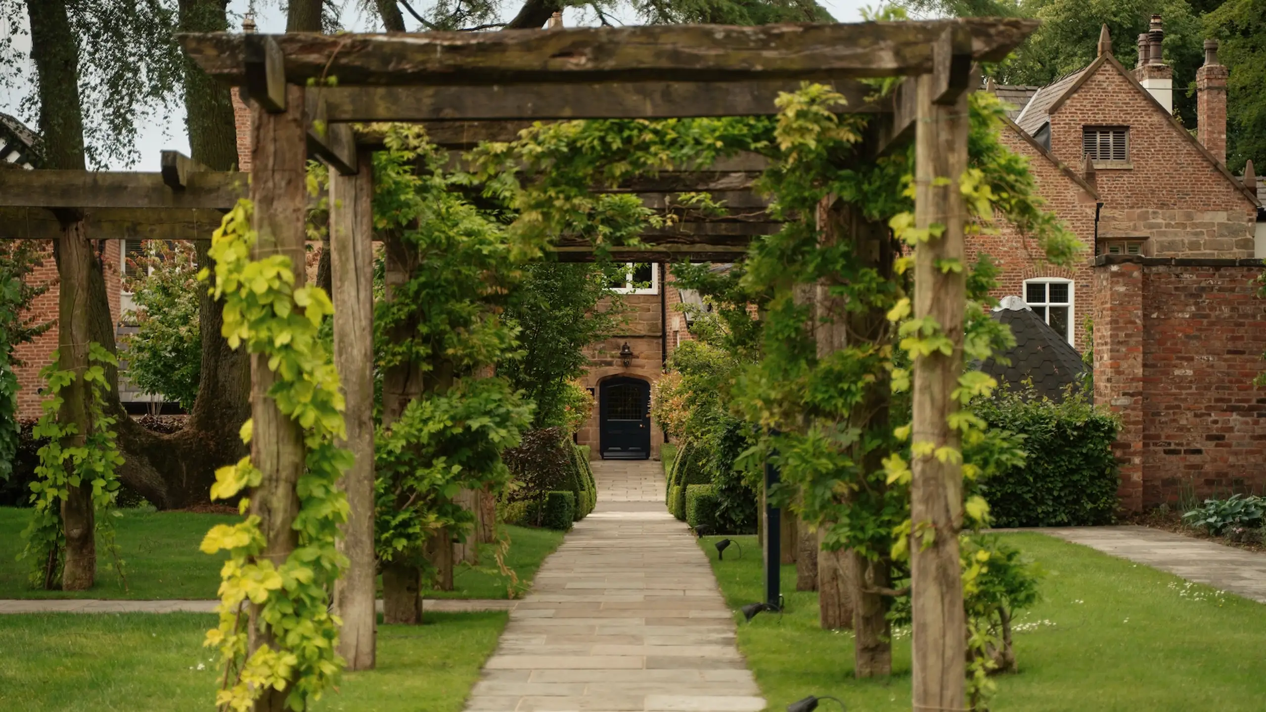 A vine-clad pergola walkway through the gardens leading to the Grade II listed Hall at Moor Hall, a wedding venue in Lancashire.