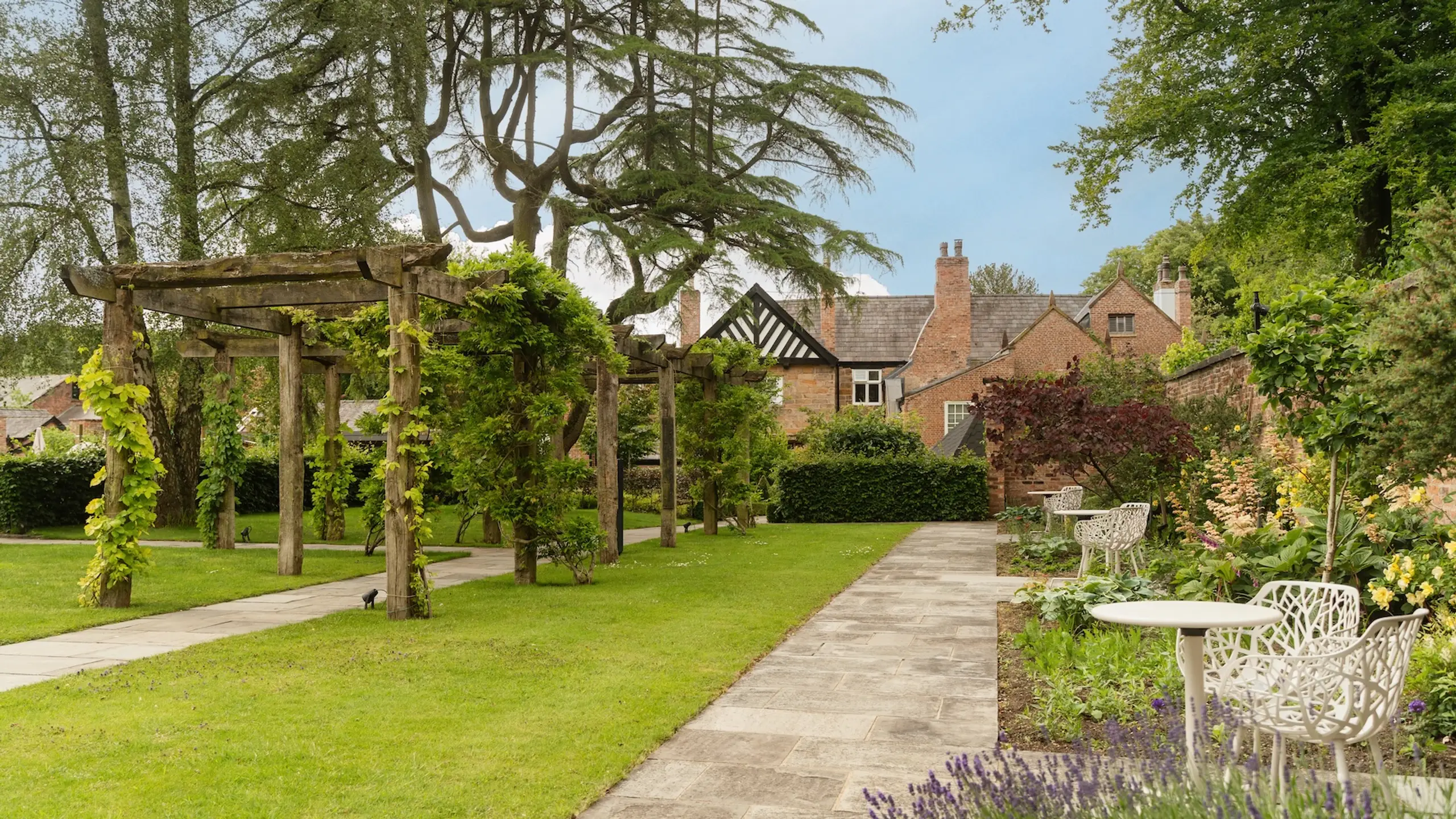 The gardens at Moor Hall, with a vine-covered pergola, lawns and seating in front of the Hall.