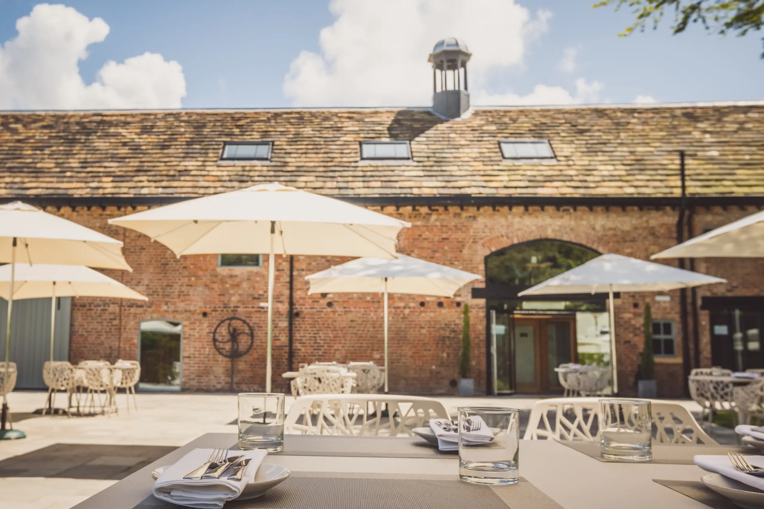 The outdoor terrace at The Barn at Moor Hall, with parasols and seating against the original brickwork.