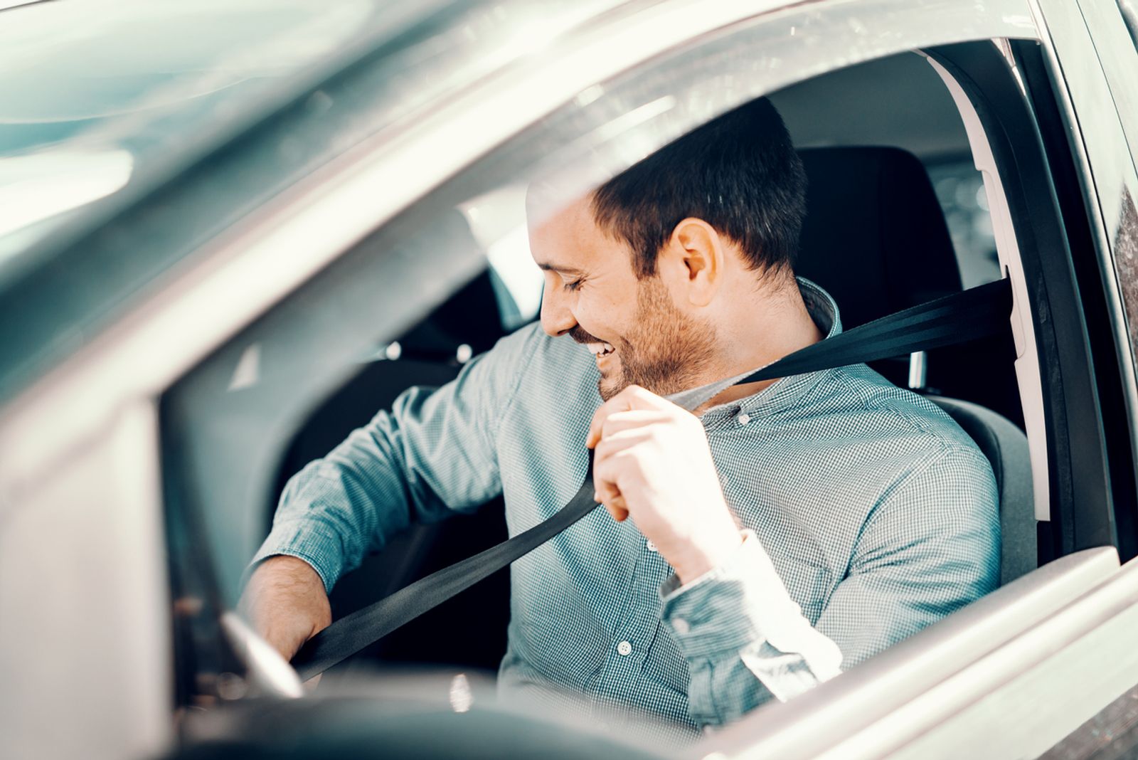 En mann som tar på seg bilbelte i bilen sin, og han er veldig glad siden han har funnet den billigste bilforsirkingen.