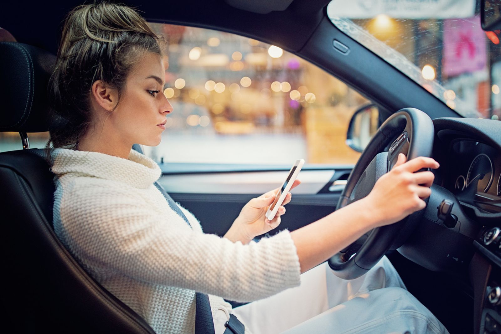 Ei dame som sitter i bilen sin og driver på mobilen, som er relevant for unge og trafikkulykker.