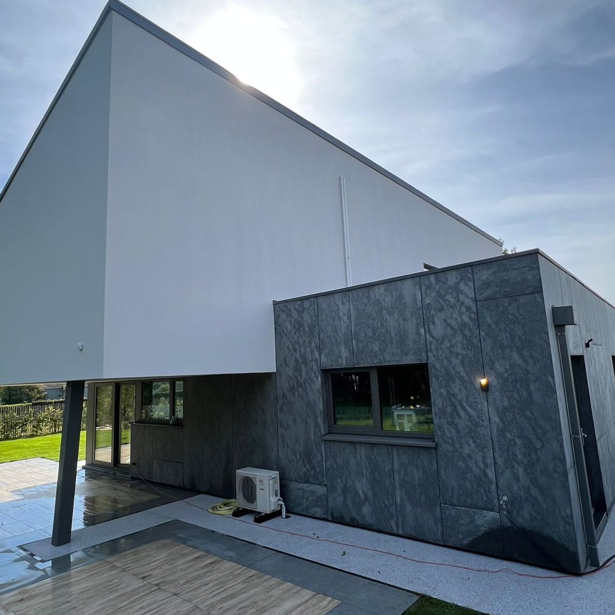 Maison contemporaine avec façade en crépi blanc et revêtement moderne, terrasse carrelée et grandes baies vitrées donnant sur le jardin.