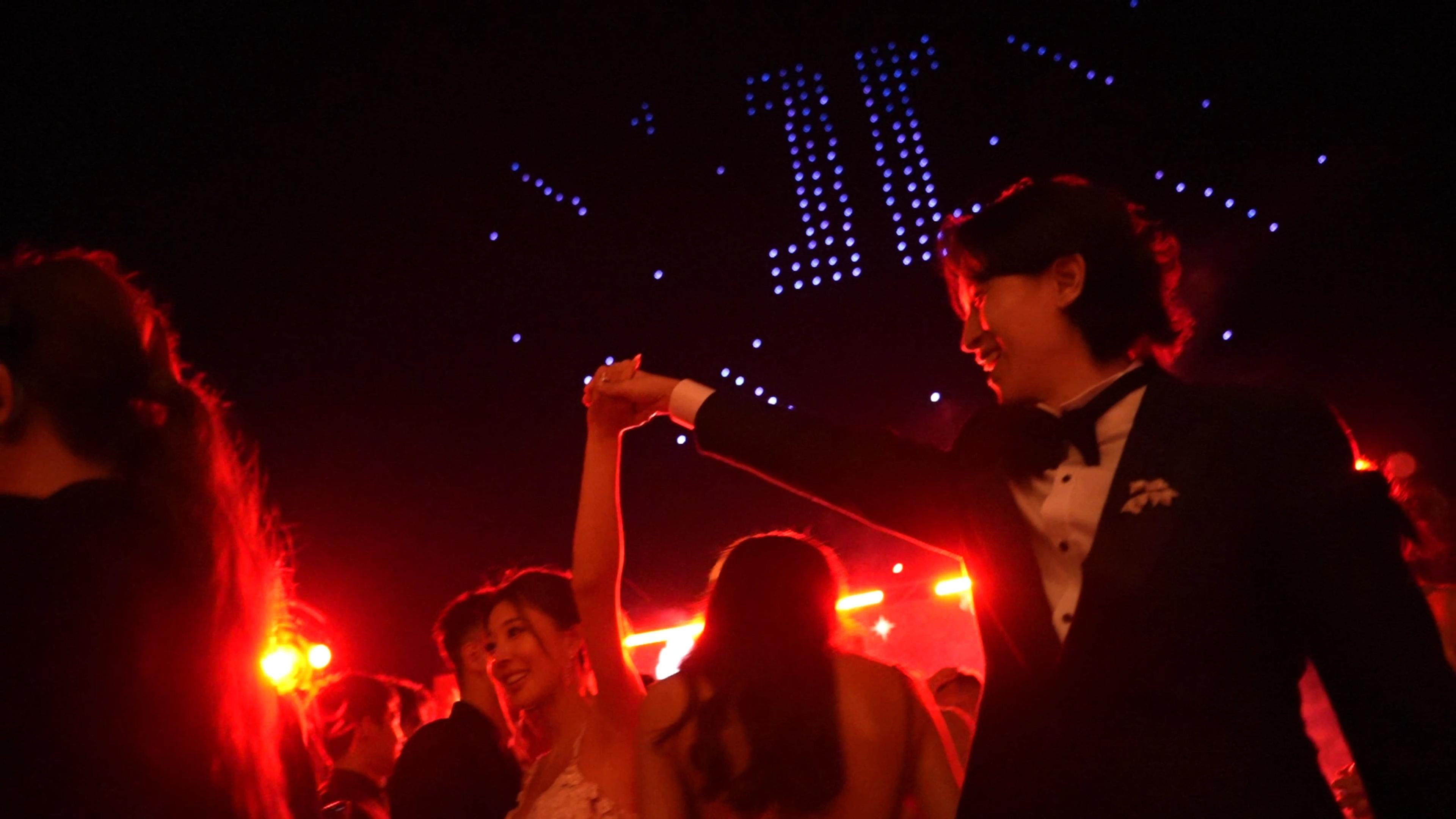 The couple celebrating with guests beneath drone lights at their Alila Villas Uluwatu wedding.