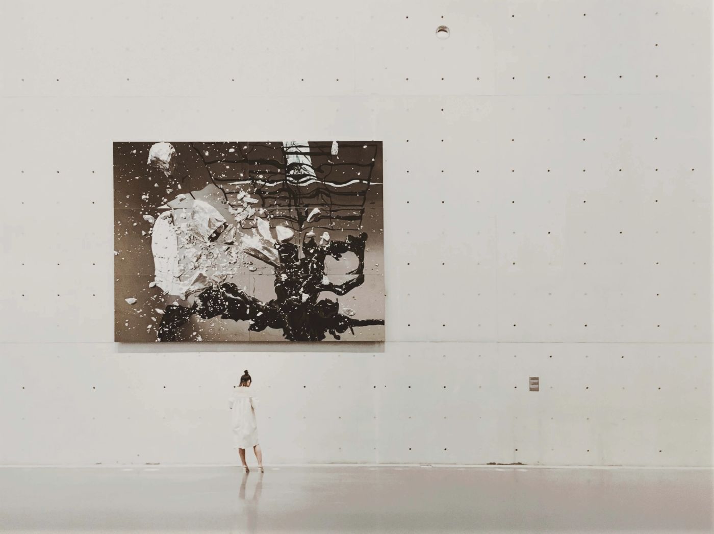 Person standing alone in a vast art gallery contemplating a large abstract painting, symbolizing the careful selection and curation process of choosing exceptional founders to back