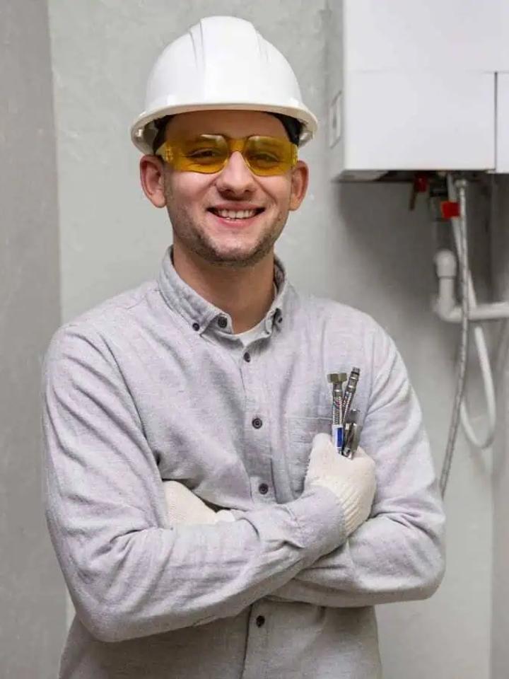 Smiling Premier Gas boiler technician in hard hat and gloves standing beside a wall-mounted boiler